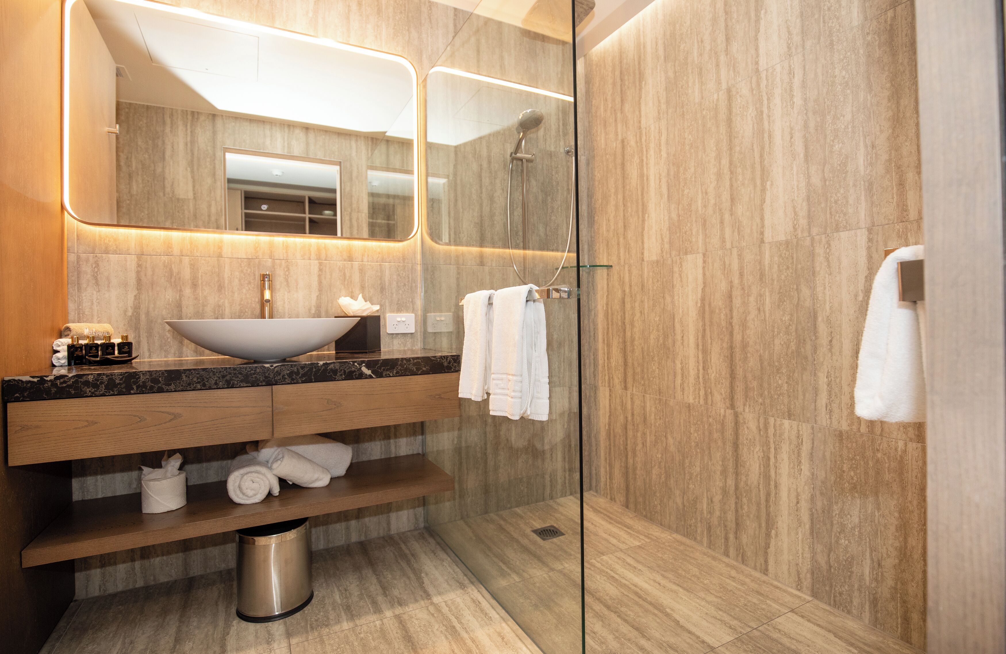 Ein modernes Badezimmer mit großem Spiegel, einem Aufsatzwaschbecken, einem Holzwaschtisch und einer Duschkabine.