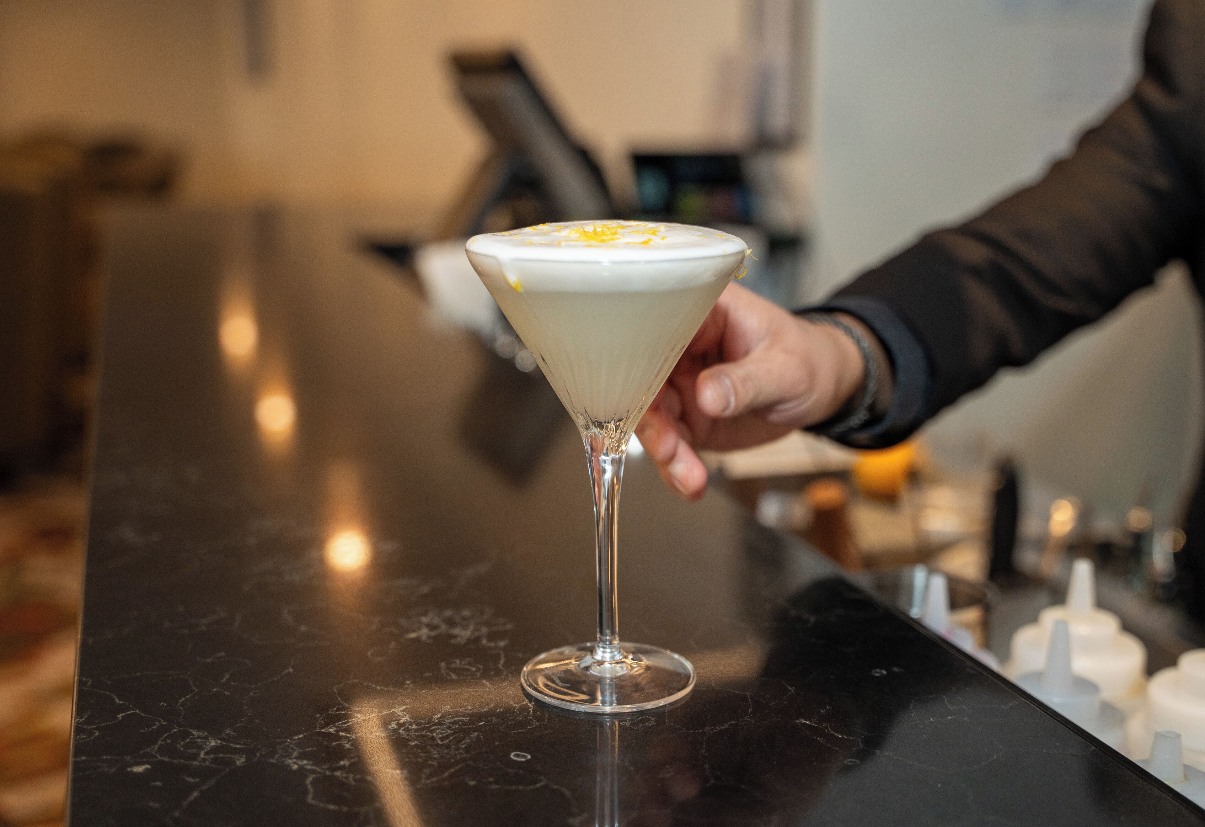 Una copa de martini con una capa cremosa, sostenida por una persona que lleva una manga oscura.