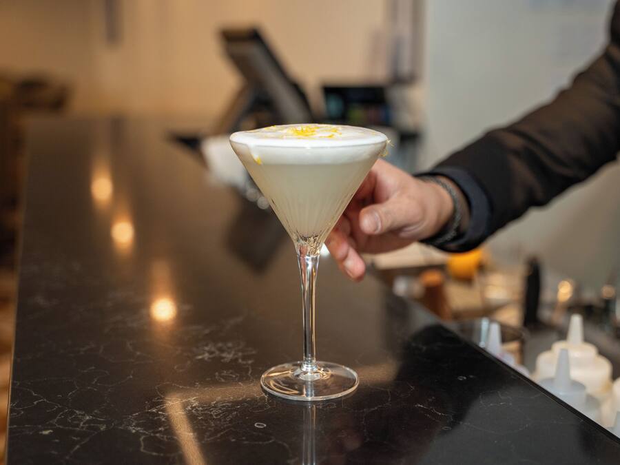 Una copa de martini con una capa cremosa, sostenida por una persona que lleva una manga oscura.
