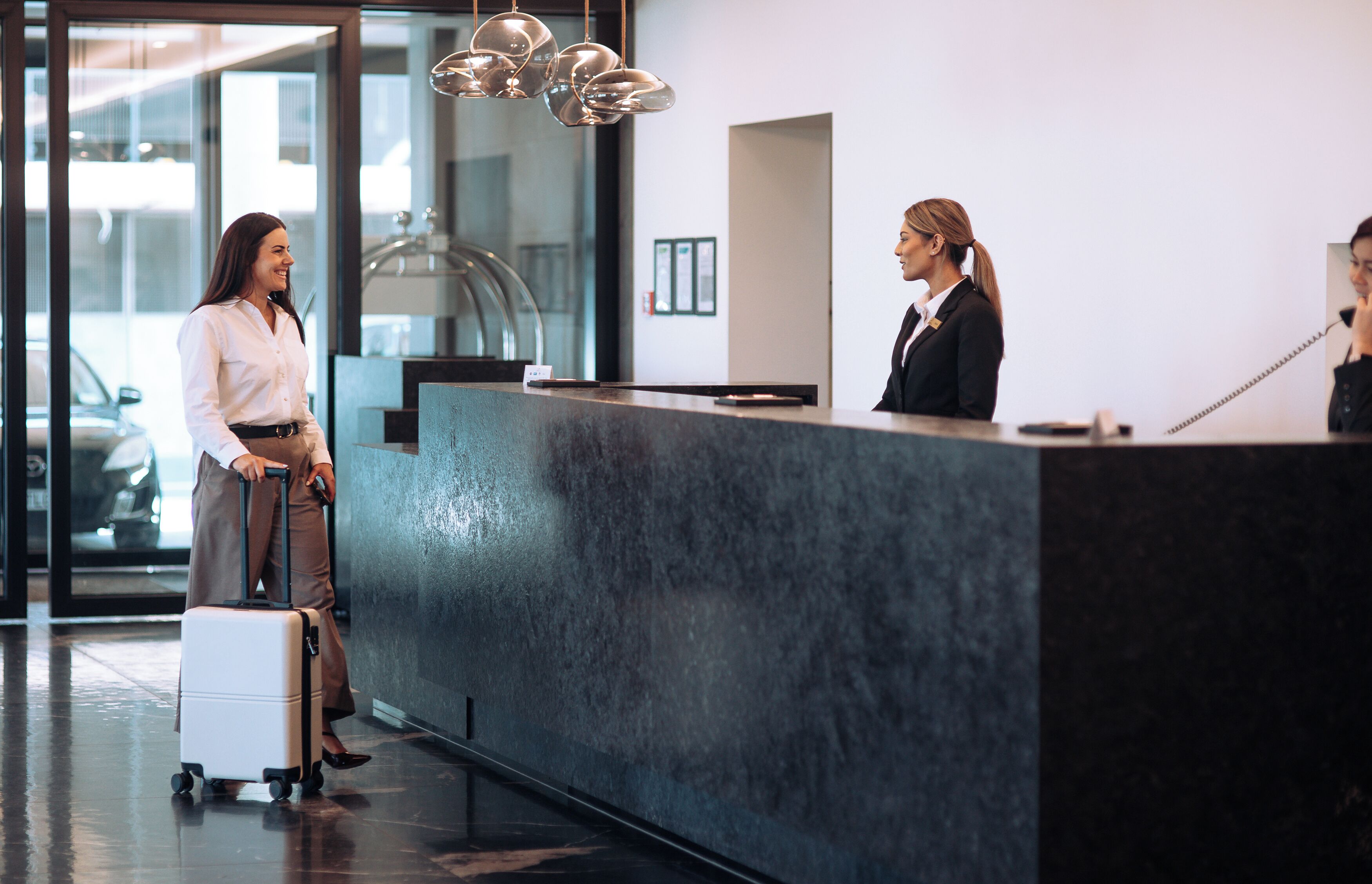 A reception desk with a modern design, a glass door entrance, and a visible car outside.
