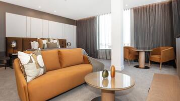 A modern hotel room with a sofa, a round glass table, and two armchairs.