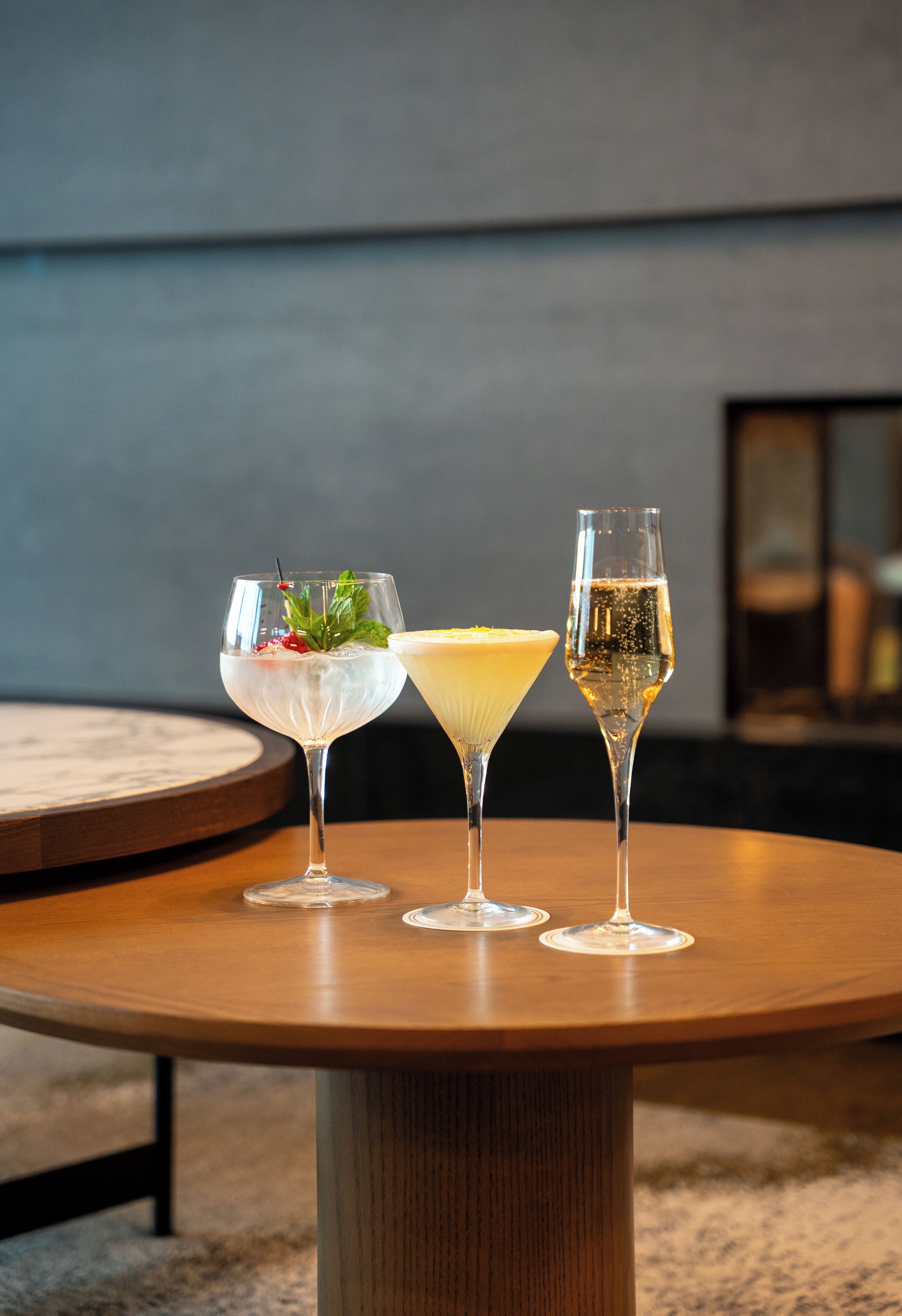 Three glasses of cocktails on a round wooden table in a modern interior setting.