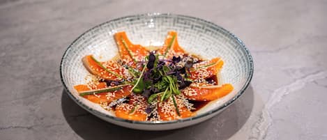 A round glass bowl with a textured rim containing a dish of food, garnished with sesame seeds and greens, on a marble surface.