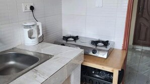 Une cuisine compacte équipée d’un évier, de deux plaques de cuisson à gaz, d’une machine à café et d’une étagère en bois située sous le plan de travail.