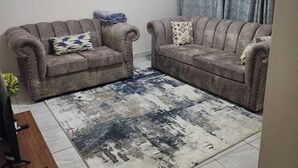 Un salon avec deux canapés, un tapis à motifs et un luminaire au plafond.