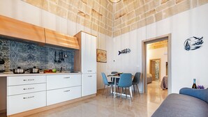 A modern kitchen with white cabinets, a dining area with blue chairs, and a living room with a blue sofa.