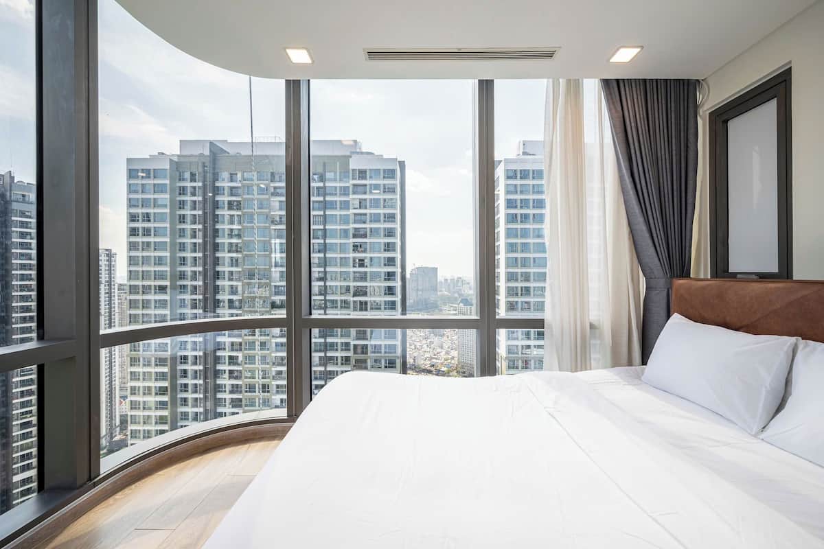Een hotelkamer met een groot bed, uitzicht op hoogbouw en een golvend raamontwerp.