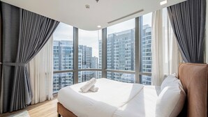 Quarto de hotel moderno com uma cama grande, vista para arranha-céus e uma janela ampla com cortinas.