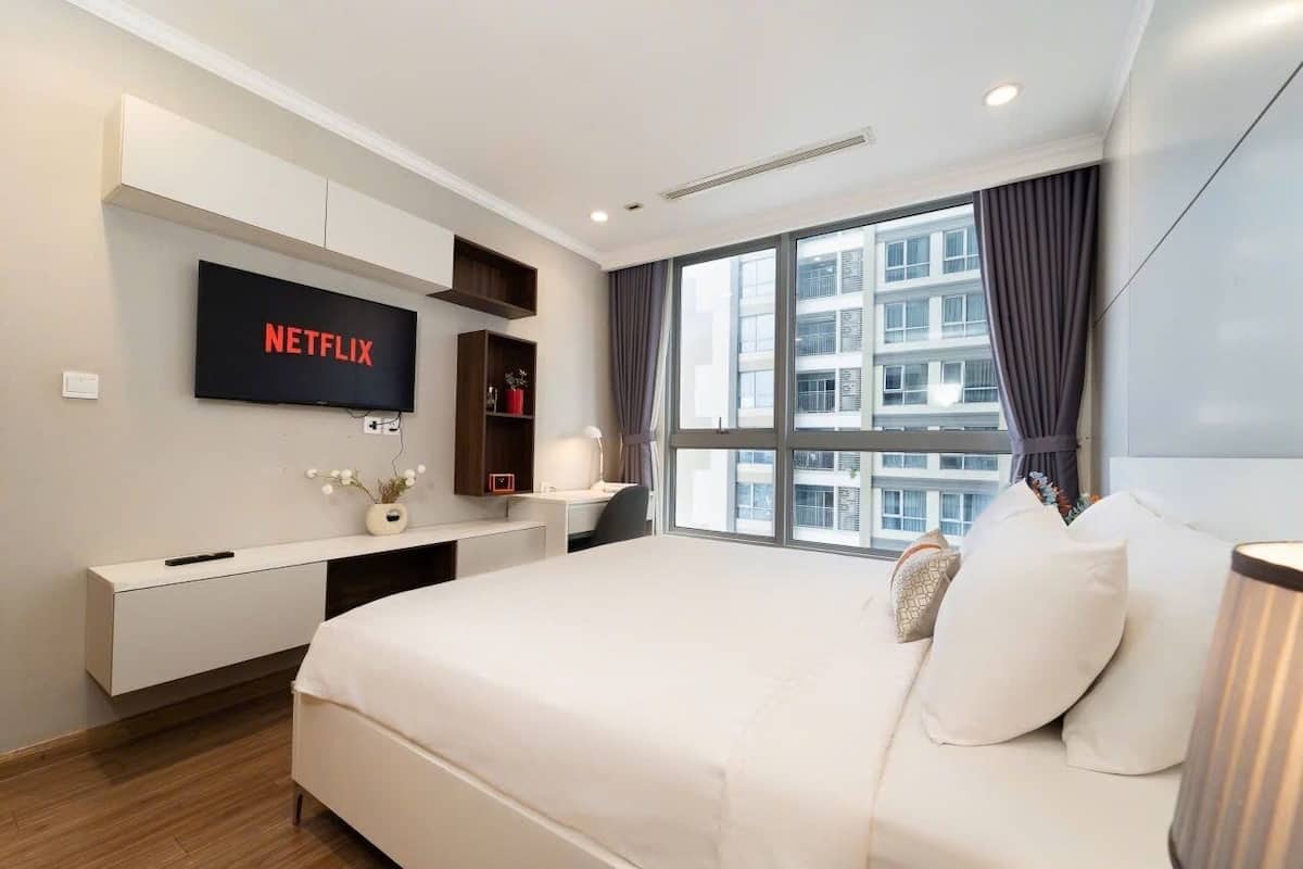 Een moderne hotelkamer met een groot bed, een bureau met een flatscreen-televisie, een raam met gordijnen en uitzicht op de stad.