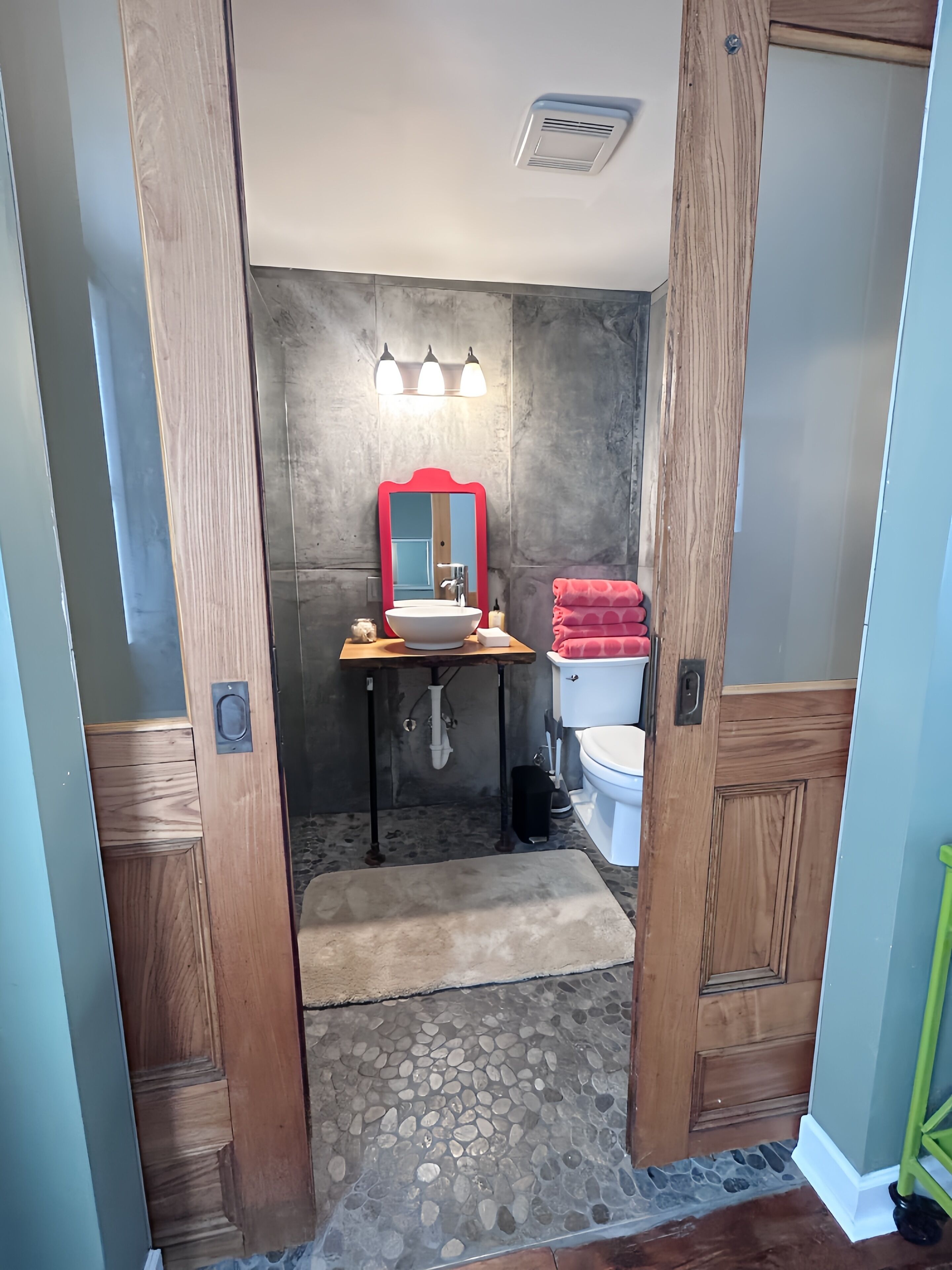 A bathroom with a wooden door, a sink with a mirror, a toilet, and a red towel.