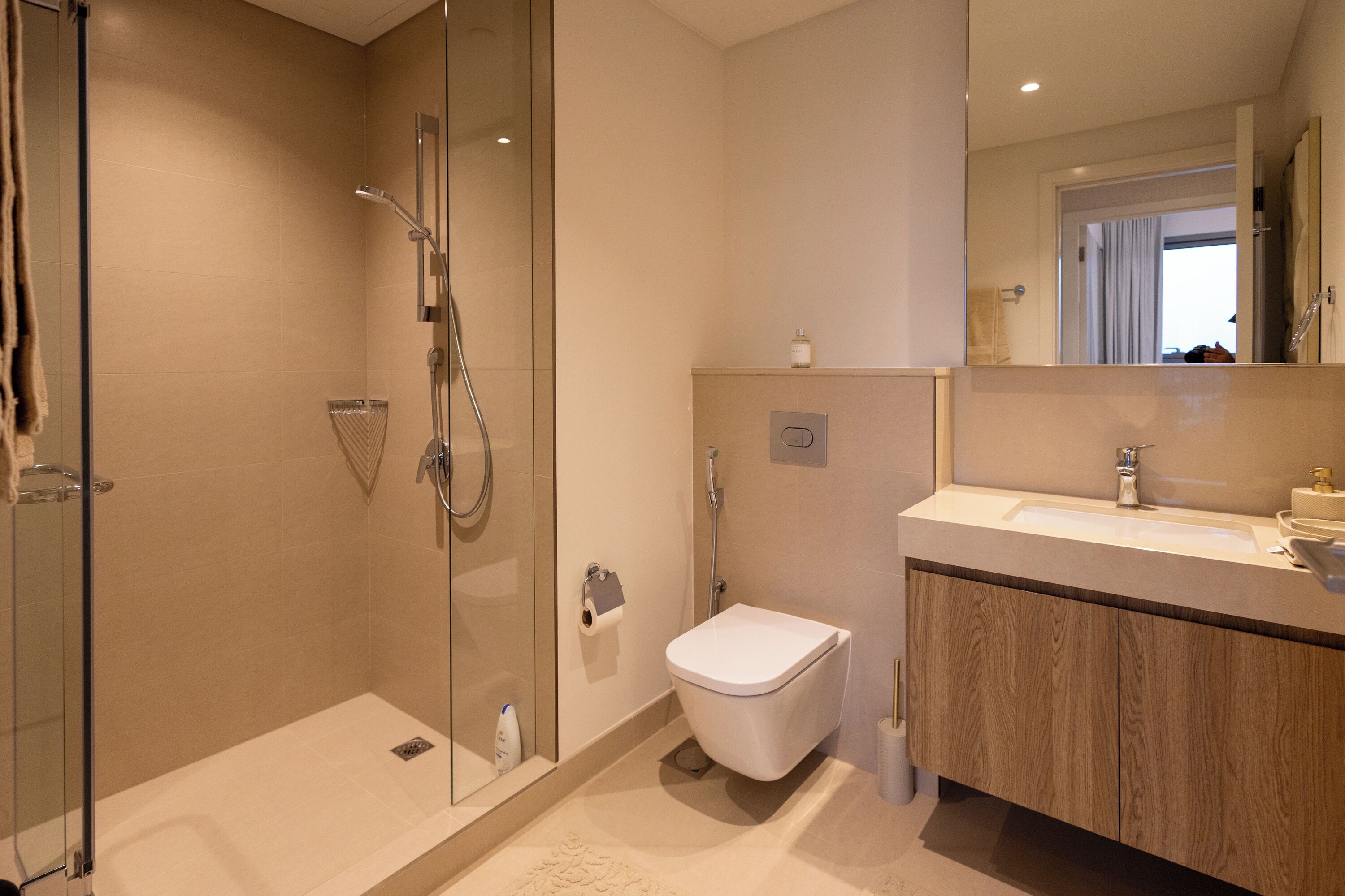 A modern bathroom with a glass-enclosed shower, a white toilet, and a wooden vanity with a sink.