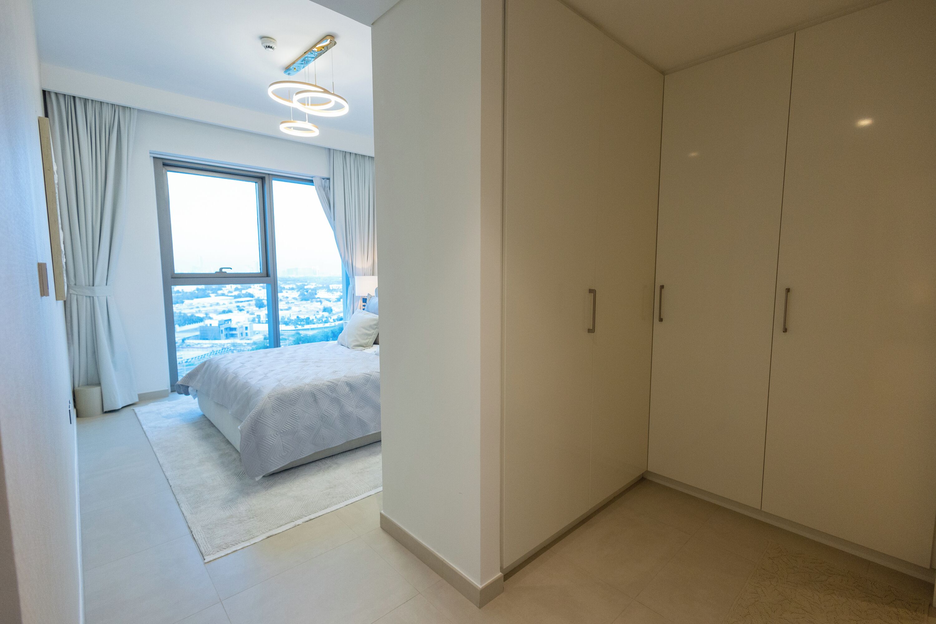 Une chambre moderne avec un grand lit, une armoire et une vue sur la ville par une grande fenêtre.