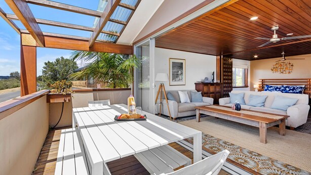 A spacious living area with a wooden ceiling, a glass ceiling, a sofa set, a coffee table, and a dining table. - El Cid - Jervis Bay Beach House (Vincentia)