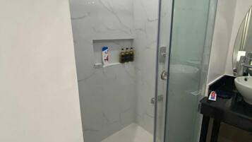 A modern bathroom with a glass-enclosed shower, a marble wall, and a black countertop with a sink.