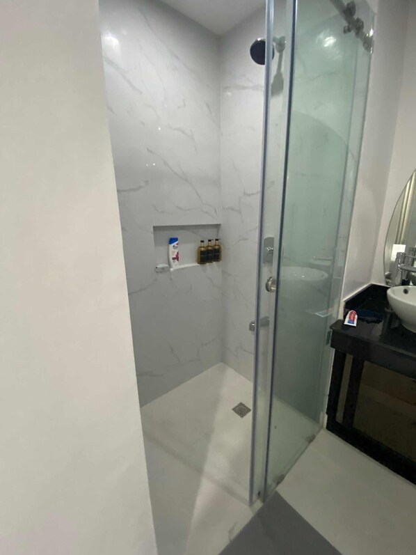 A modern bathroom with a glass-enclosed shower, a marble wall, and a black countertop with a sink.