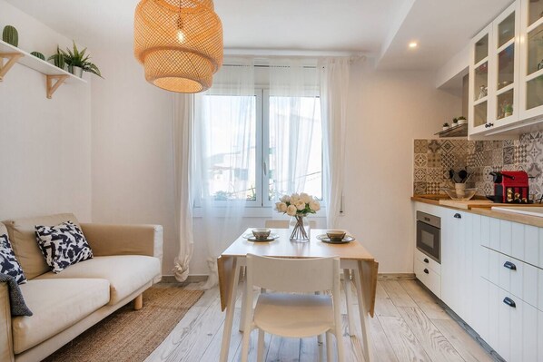 A modern kitchen with white cabinets, a dining table, and a hanging light fixture.