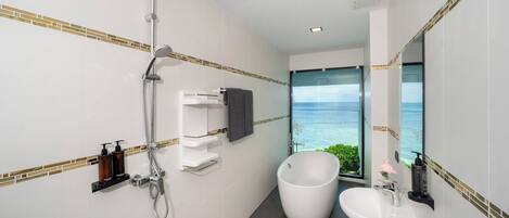 A modern bathroom with a shower, a bathtub, and a sink. It features a large window with a view of the ocean.