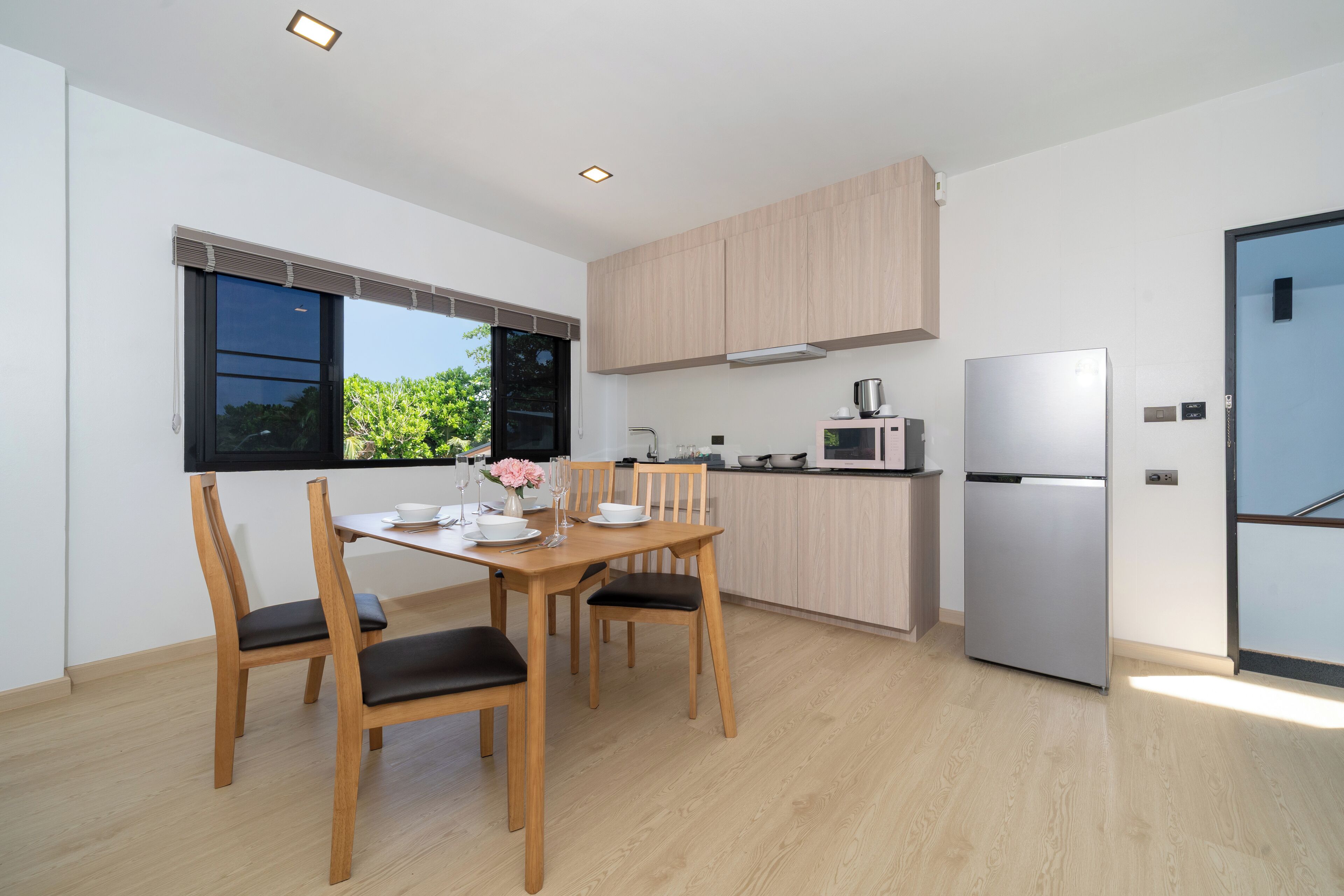 A modern kitchen with wooden cabinets, a stainless steel refrigerator, and a dining area with a table and chairs.