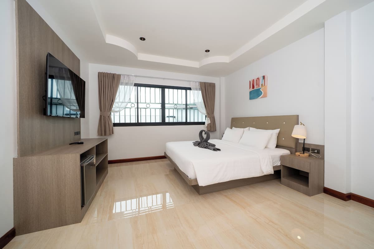 A hotel room with a bed, a TV mounted on the wall, a nightstand, and a window with curtains.