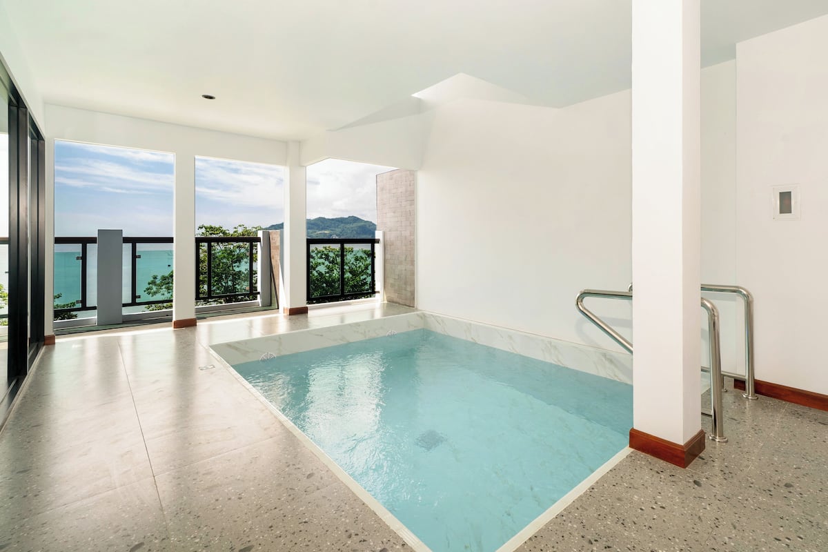 A spacious indoor swimming pool with clear views of the sea and mountains through large windows.