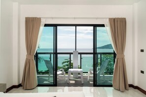 A room with a large sliding glass door leading to a balcony with a view of the sea. There is a small table and two chairs on the balcony. - The Hideout Beachfront (Patong)