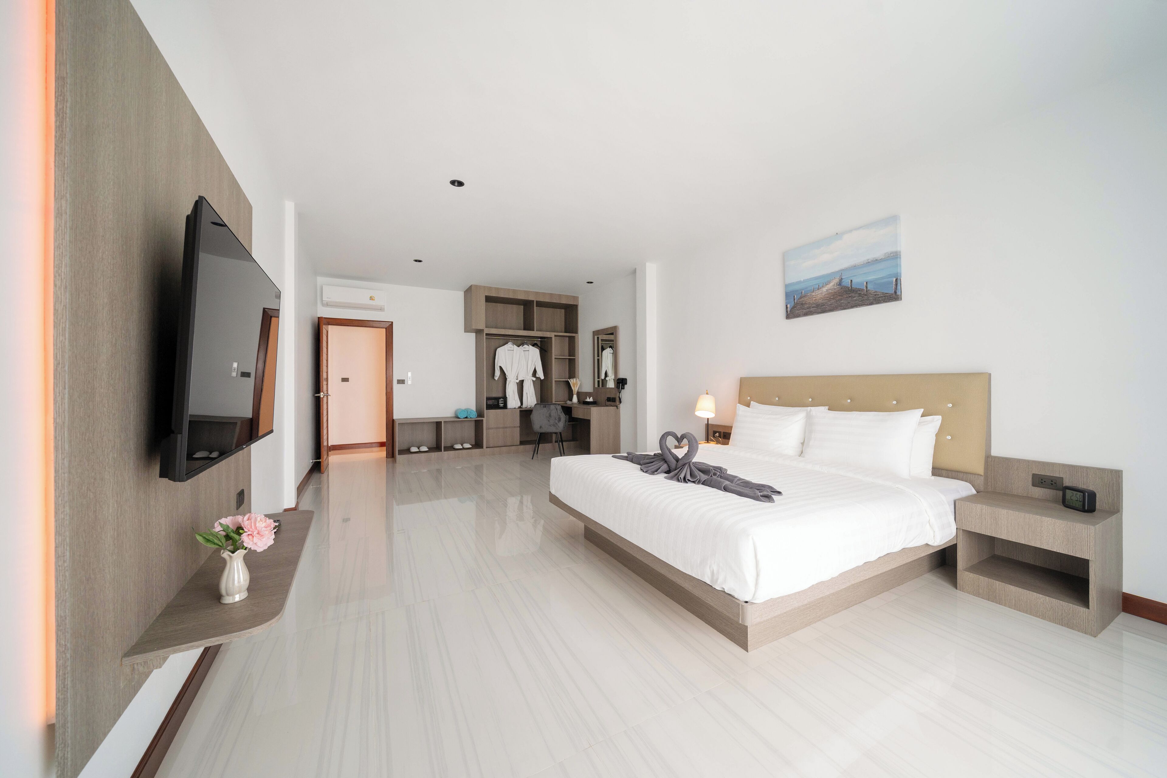 A modern hotel room with a large bed, bedside tables, a flat-screen TV, a desk with a chair, and a wardrobe.