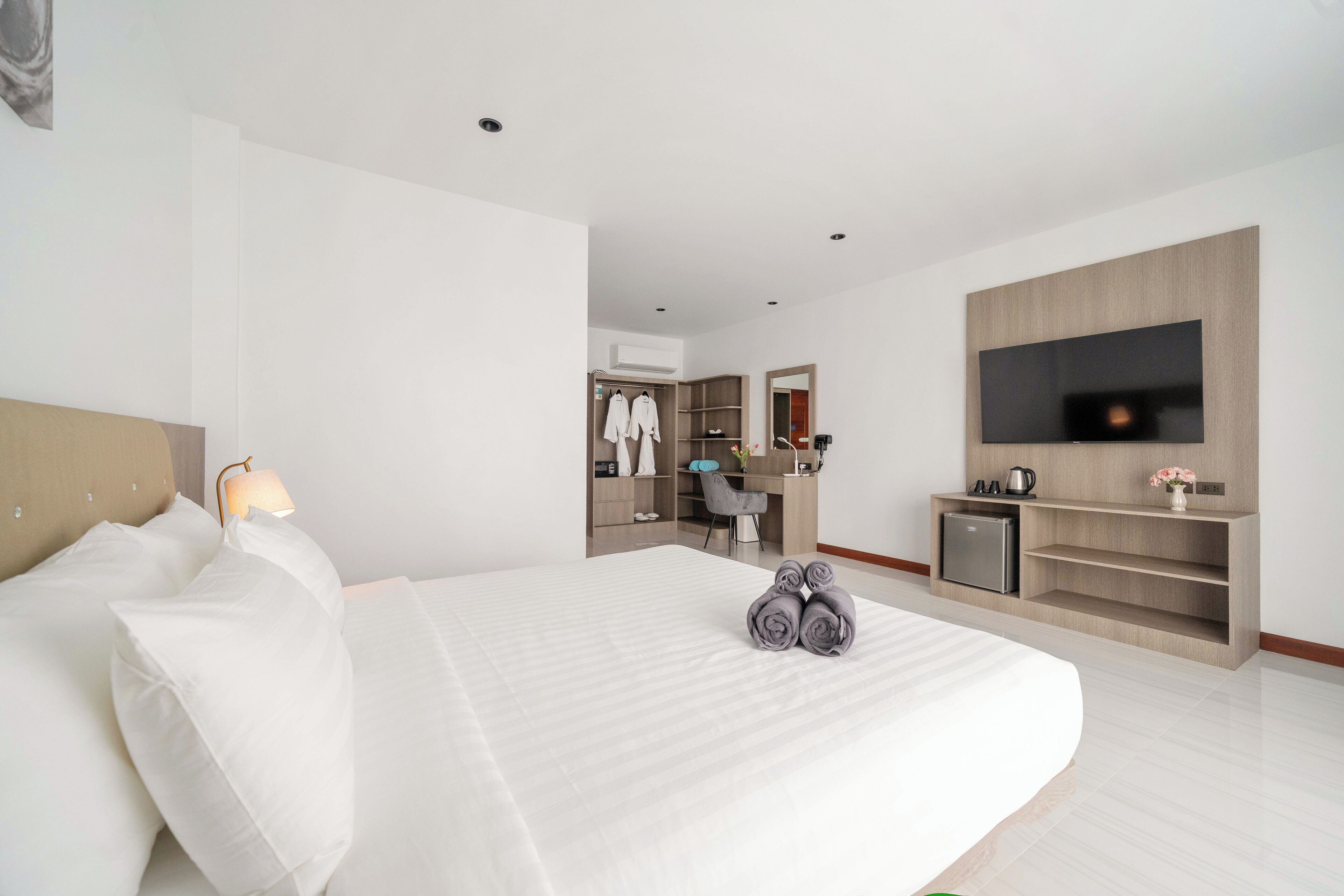 A modern hotel room with a large bed, a desk, a TV, and a wardrobe.