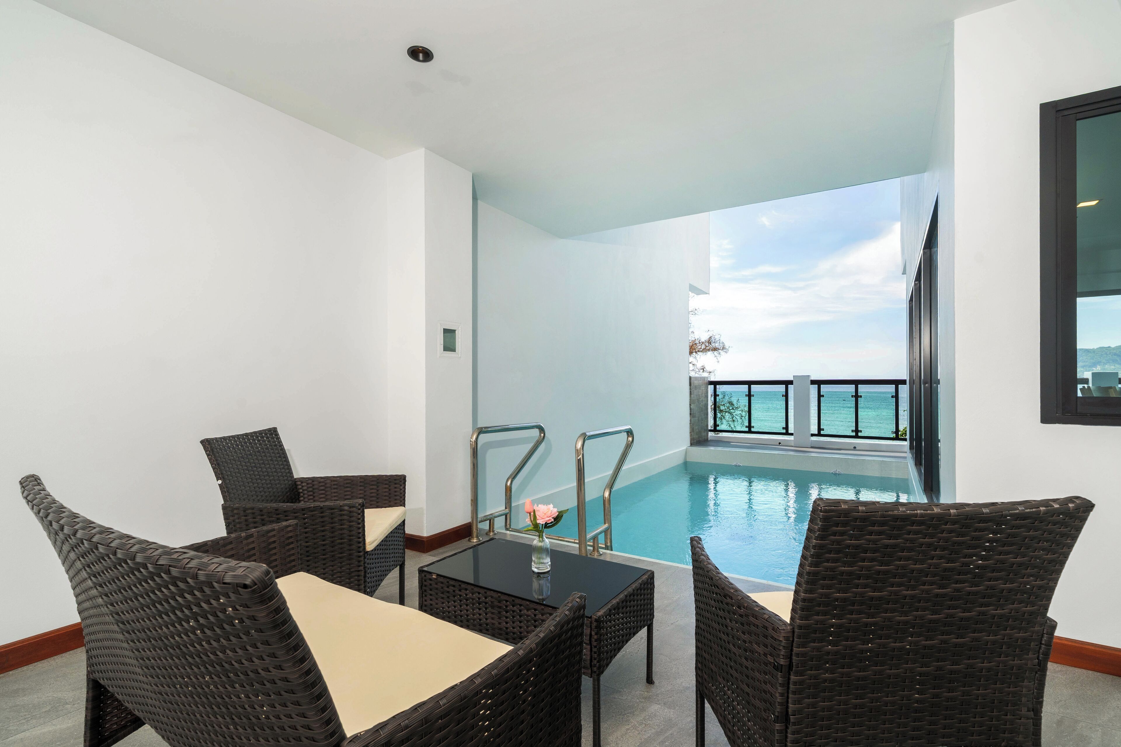 A balcony with wicker furniture, a pool, and a view of the ocean.