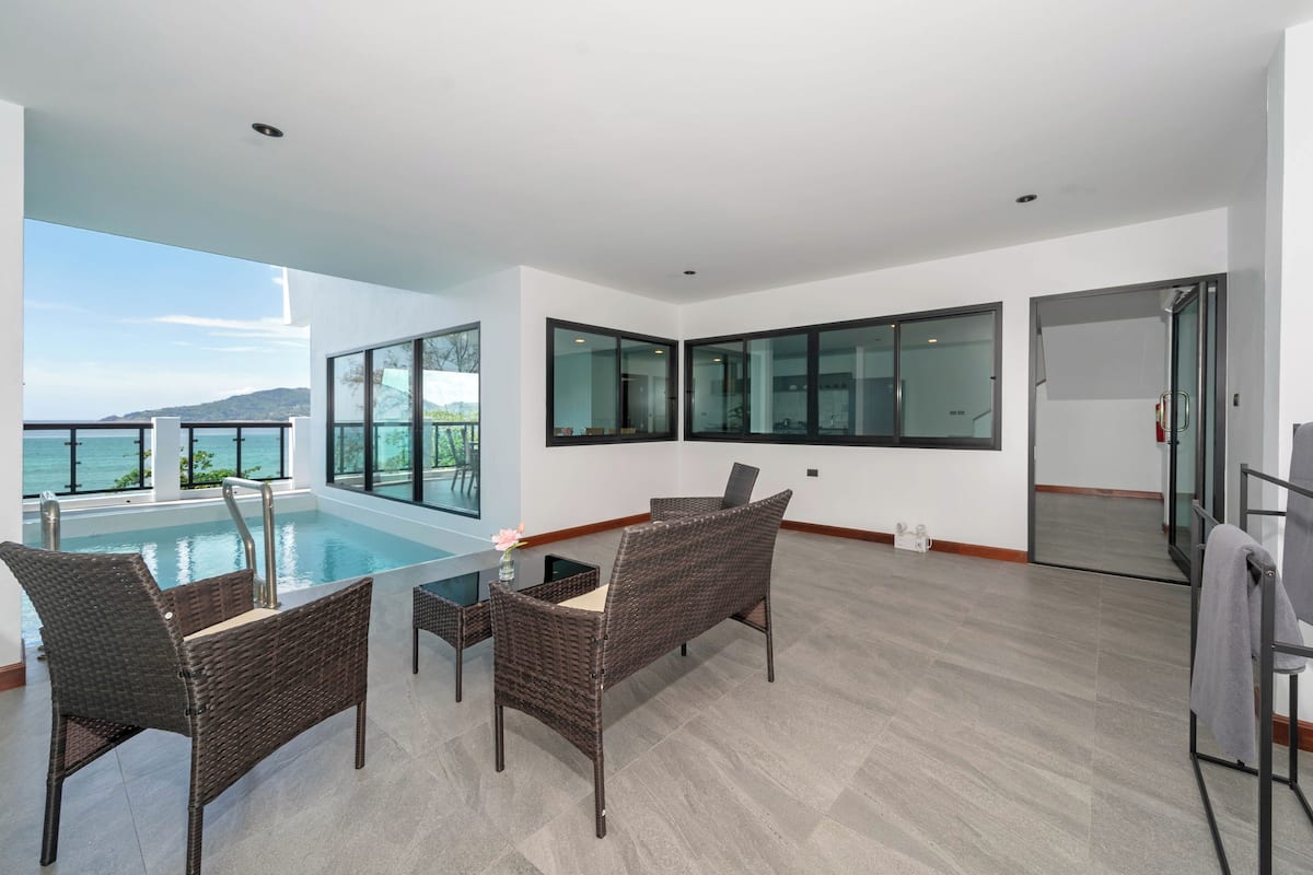 A modern room with a pool, wicker furniture, and large windows offering a view of the sea.
