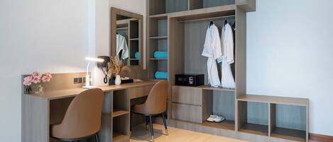 A modern room with a built-in desk, two chairs, a mirror, and a walk-in closet with shelves and hanging space.