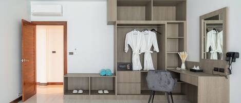 A modern bedroom with a wooden wardrobe, a desk, and a chair. There is a mirror on the wall and a door leading to another room.