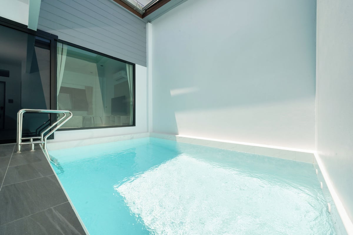 A modern indoor swimming pool with a glass wall, a metal pool ladder, and a tiled floor.