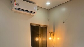 Et hotelværelse med en seng, et vindue, en aircondition og en vægmonteret lampe.