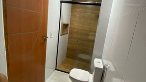 Et badeværelse med toilet, bruseområde og en trædør.
