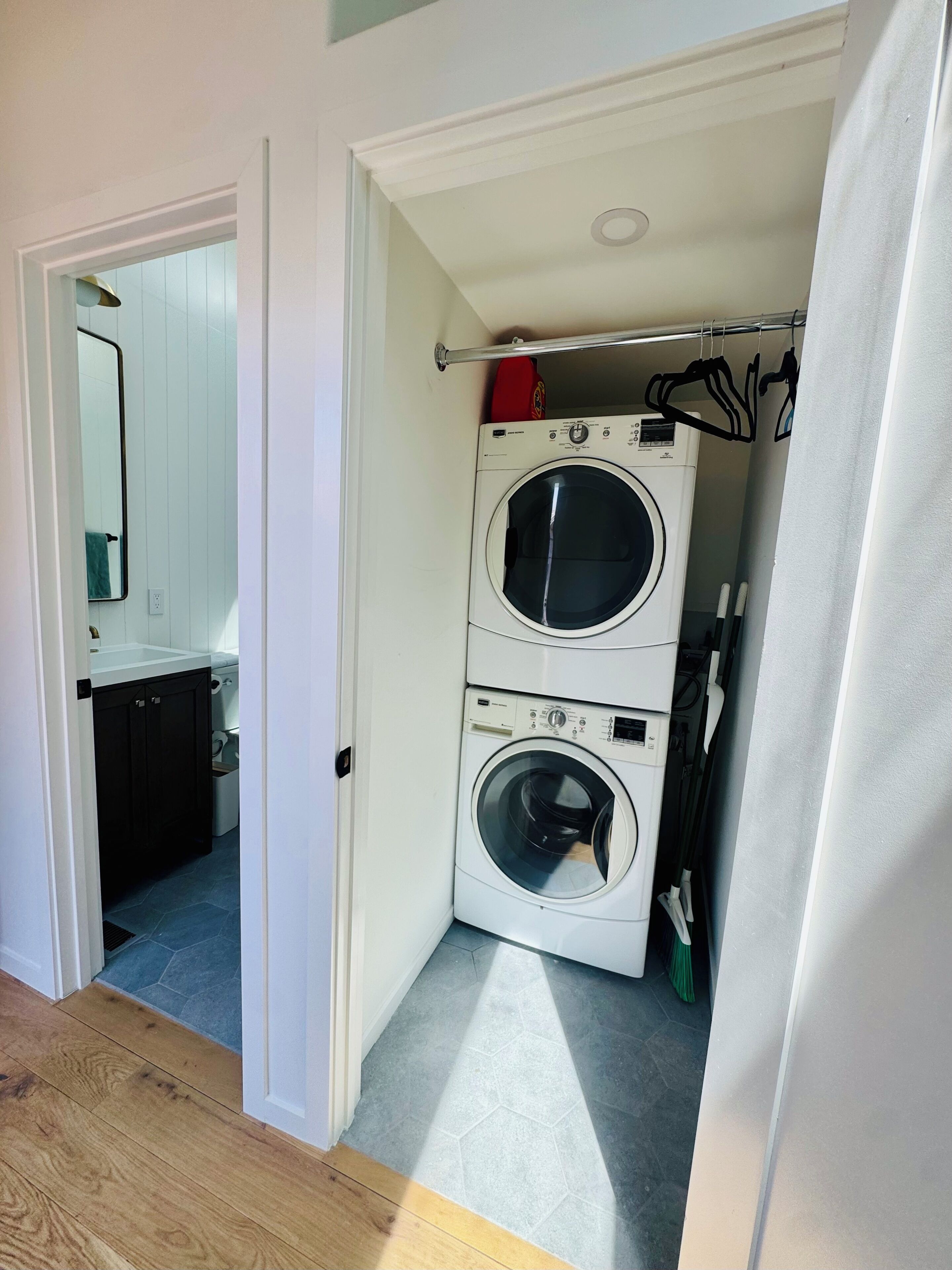 A laundry room with two stacked washing machines, a drying rack, and a mirror.