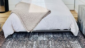 Quarto moderno com uma cama grande, roupa de cama branca e um tapete estampado.