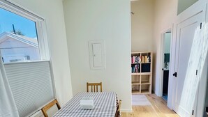 Uma área de refeições com uma mesa posta para dois, cadeiras de madeira, toalha xadrez e uma janela com persianas.