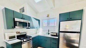 Uma cozinha moderna com armários verde-água, eletrodomésticos de aço inoxidável e uma grande janela que oferece iluminação natural.