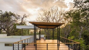 A modern outdoor deck with a wooden floor and metal railings, surrounded by trees and a clear sky. - Spacious 5-bedroom luxe, fully equipped villa minutes walk to Pelada beach (Nosara)