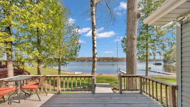 A wooden deck with a table and chairs, overlooking a lake with a boat docked in the background.