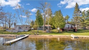 A lakeside property with a dock, a house with a porch, and a small bridge connecting to another building.
