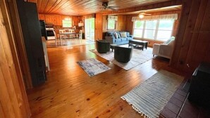 A spacious wooden cabin interior with a dining area, living room, and large windows.