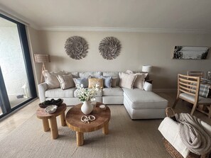 A living room with a sofa, two round wooden tables, a vase with flowers, and a painting on the wall.