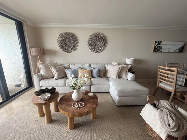 A living room with a sofa, two round wooden tables, a vase with flowers, and a painting on the wall.
