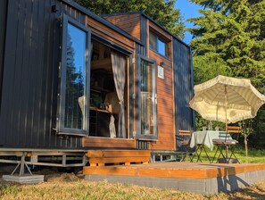 Una cabaña moderna con fachada de madera, puerta corrediza de vidrio y un pequeño espacio exterior con sombrilla.