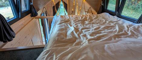 A cozy room with a bed, large windows, and a view of the outdoors.