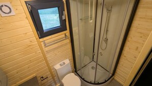Un baño pequeño con inodoro, ducha con mampara de vidrio y una ventana.