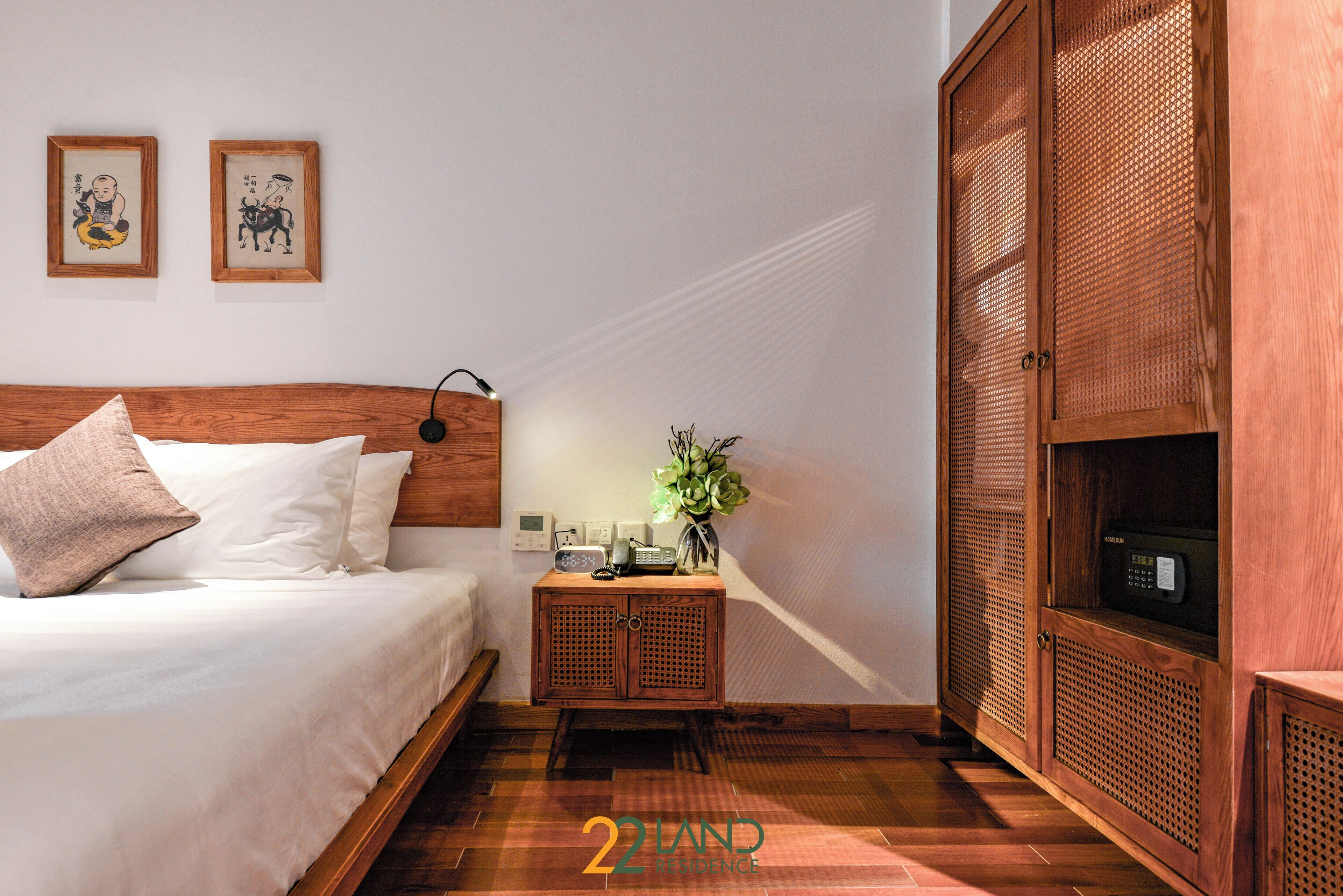 Une chambre à coucher avec une tête de lit en bois, une table de chevet avec une lampe, une horloge et une petite plante. Un placard avec un motif tissé se trouve sur le côté droit.
