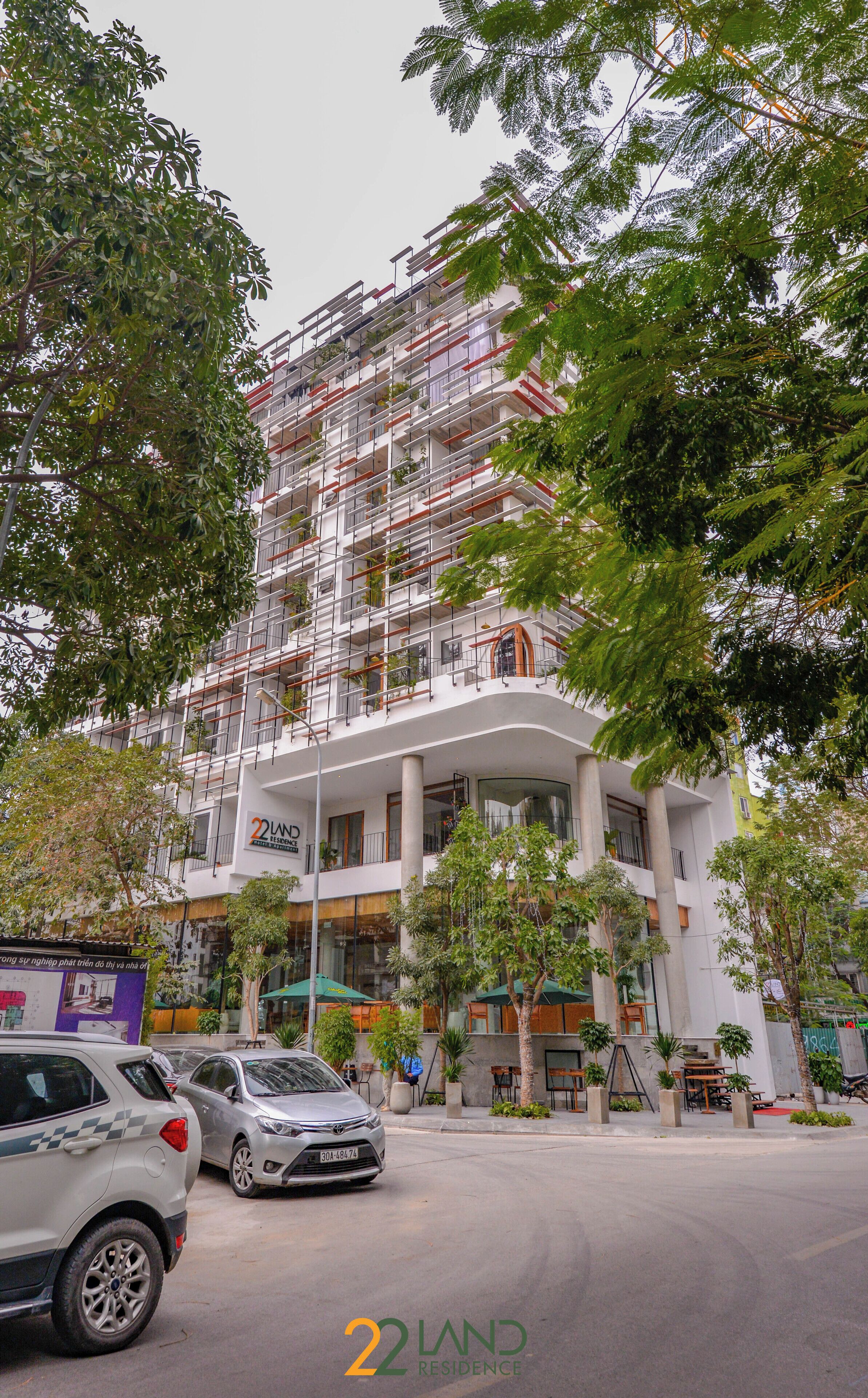 Un immeuble à plusieurs étages doté de balcons, une enseigne indiquant « 22 LAND RESIDENCE », et une rue devant, où sont garées des voitures.