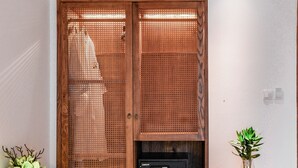 A wooden wardrobe with a perforated door, a small shelf with a black object, and a potted plant on a wooden table beside it. - 22 Land 50 Truong Cong Giai Hotel (Hanoi)